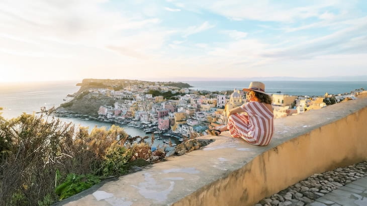 A woman sitting on a wall looking out at the view over the coast